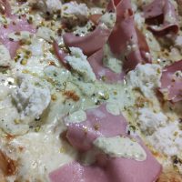 La Pizza Pistache est une spécialité élégante et audacieuse, qui célèbre les saveurs raffinées et subtiles de la Méditerranée. Garnie de crème de pistache onctueuse, de mozzarella fondante et de tranches de mortadelle, elle est finalisée à la sortie du four avec des éclats de pistache croquants et du fior di latte crémeux, pour une touche finale douce et parfumée. Chez Sancta Maria 1187, nous préparons cette pizza avec le plus grand soin, en la cuisant sur pierre de lave pour une pâte croustillante et légère, parfaite pour sublimer chaque ingrédient. Dans notre cadre historique, situé dans l’ancien réfectoire voûté de la chapelle Notre Dame des Eaux à Balaruc-les-Bains, cette Pizza Pistache vous promet une expérience gustative unique et pleine de caractère. En été, profitez de notre jardin fleuri pour savourer cette spécialité en plein centre-ville, à seulement deux minutes du bord de l’étang, dans une ambiance conviviale et méditerranéenne, idéale pour apprécier les saveurs subtiles de cette pizza exceptionnelle.